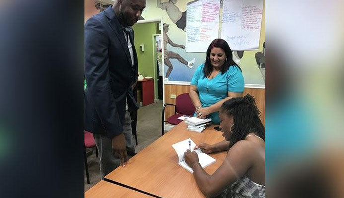 WORDS OF WISDOM: Four-time Olympic medallist Lauryn Williams, right, signs a copy of her book The Oval Office for national football coach Dennis Lawrence as Trinidad and Tobago Olympic Committee executive member Nadine Khan looks on. The book-signing took place at Olympic House on Wednesday. —Photo courtesy: MELANIE GULSTON
