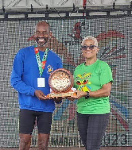 St Lucian Jason Sayers, left, collects his trophy from TT Olympic Committee president Diane Henderson after winning the TT Marathon at the Queen's Park Savannah, Port of Spain on Sunday. (Image obtained at newsday.co.tt)